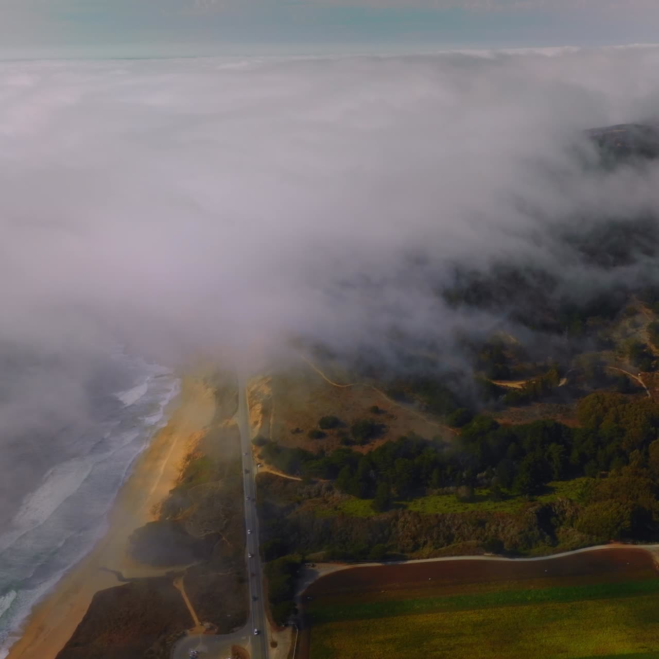 Beautiful coast with sandy beach, rocks and meadows in Montara, California, USA. Thick white fog spreading on the land from water. Aerial view
