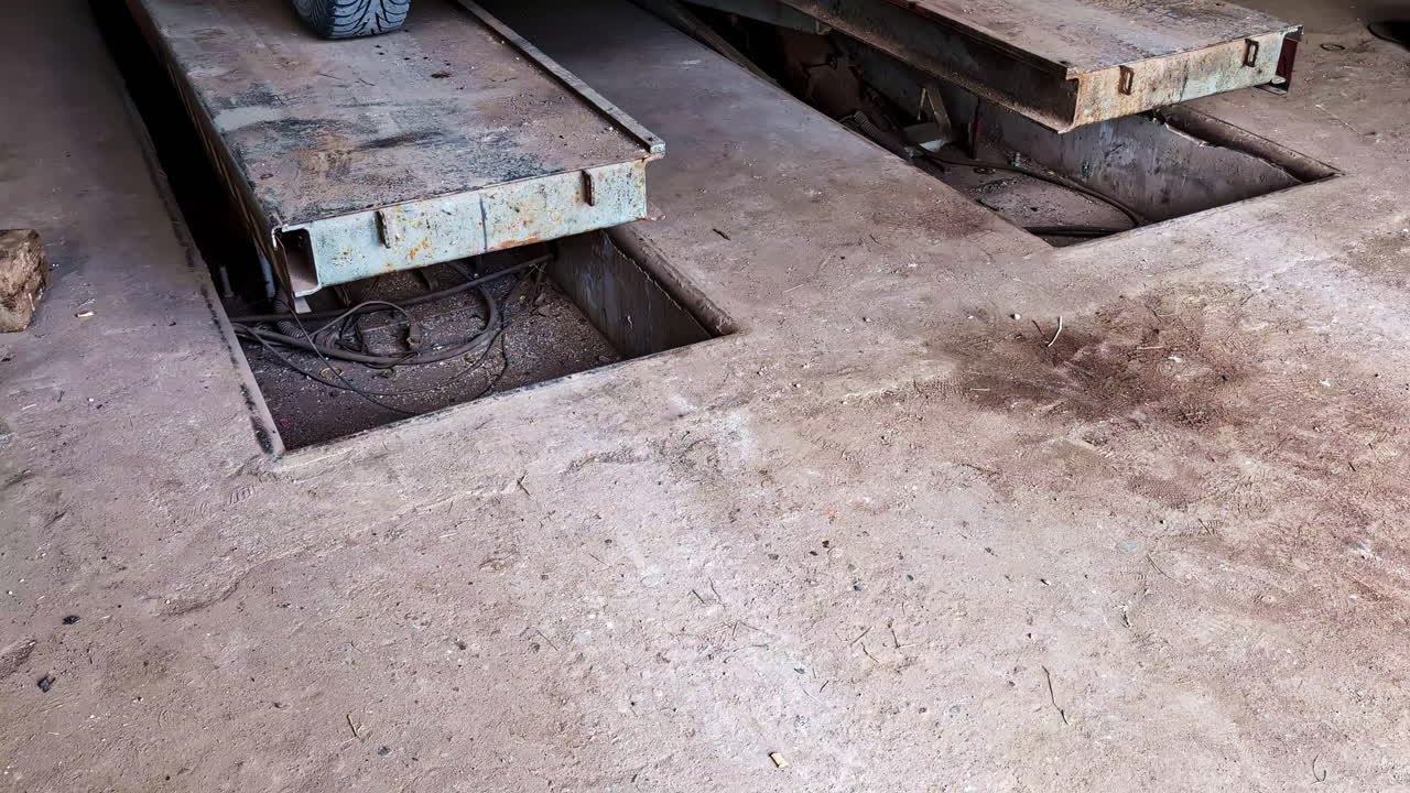 Scissor car lift platform slowly lowers inside a dimly lit rural garage