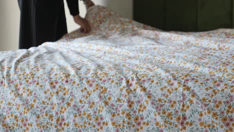 a woman making a bed with floral bedding