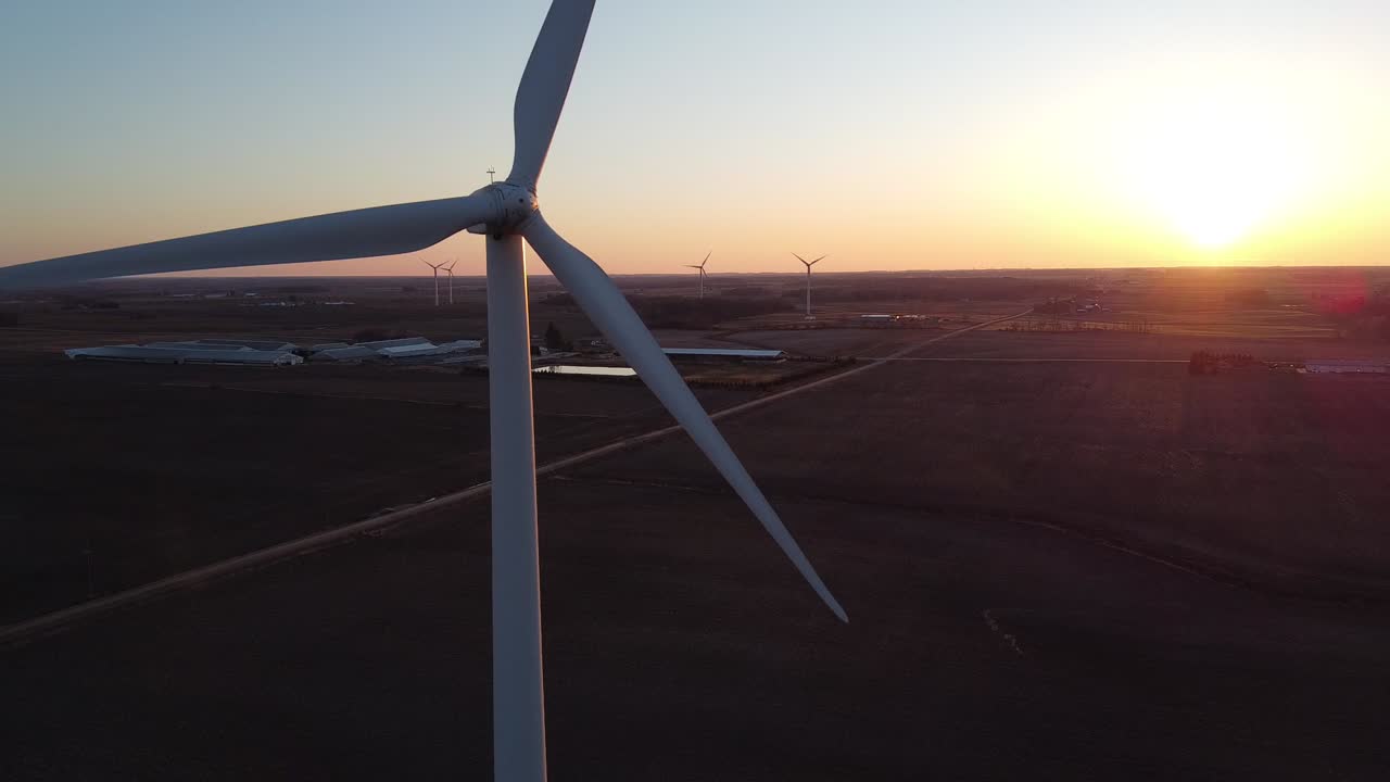 A white, tall industrial windmill spinning in the sunset in Ubly, Michigan - aerial
