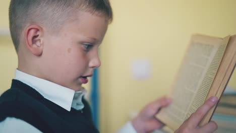 boy-in-vest-reads-textbook-sitting-at-table-in-light-room