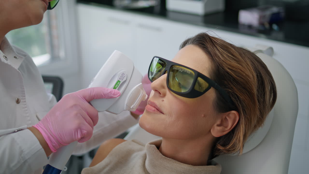 Kosmetikerin führt Gesichtsbehandlung mit Lasergerät in der Klinik in Nahaufnahme durch