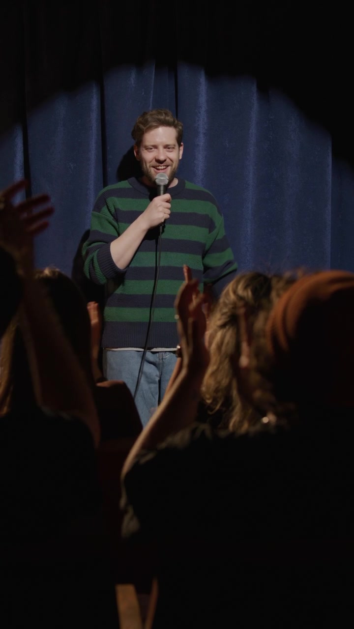 Standup-komiker går inn på scenen og hilser på et applauderende publikum