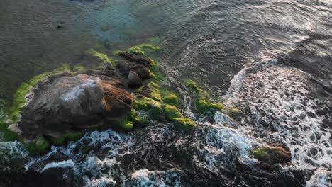 aerial shot around rock in the sea at sunset