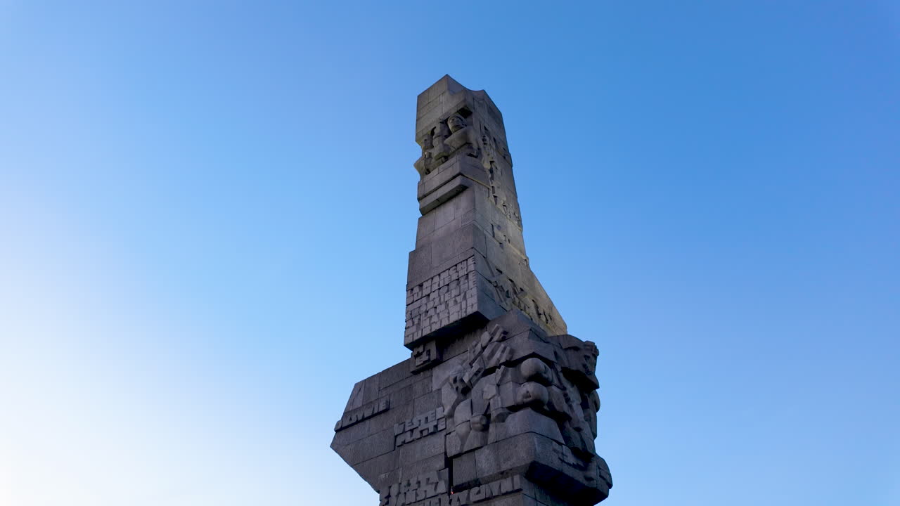 Close-up of the Westerplatte Monument against a clear blue sky, highlighting the rough-cut texture and heroic bas-relief carvings