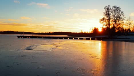 timelapse-of-jetty-dock-and-golden-sunset-in-the-winter,-water-making-the-thin-ice-pulsate-and-jump