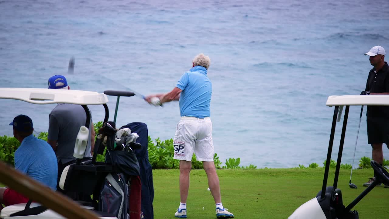 Older male golfer hitting a golf ball with a driver on a golf course by the ocean in Curacao, Caribbean