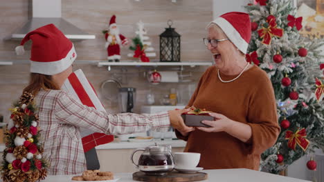 Glückliche-Familie-Mit-Weihnachtsmütze,-Die-Sich-Gegenseitig-Mit-Einem-Weihnachtsgeschenk-In-Der-Verpackung-überrascht