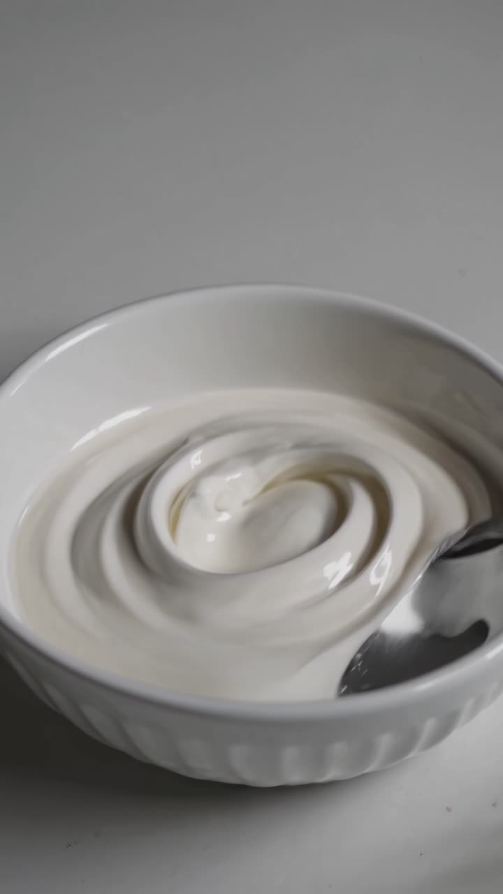 Close-up video shot of a bowl of creamy yogurt with a spoon, showcasing a smooth, swirled texture