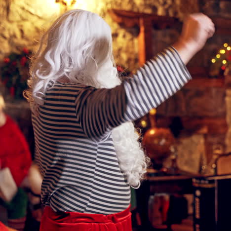 santa claus is making his morning exercises in specially decorated room. boy and girl elves in the background are holding his costume. christmas spirit concept close up video. christmas eve. new year is coming. side view video.