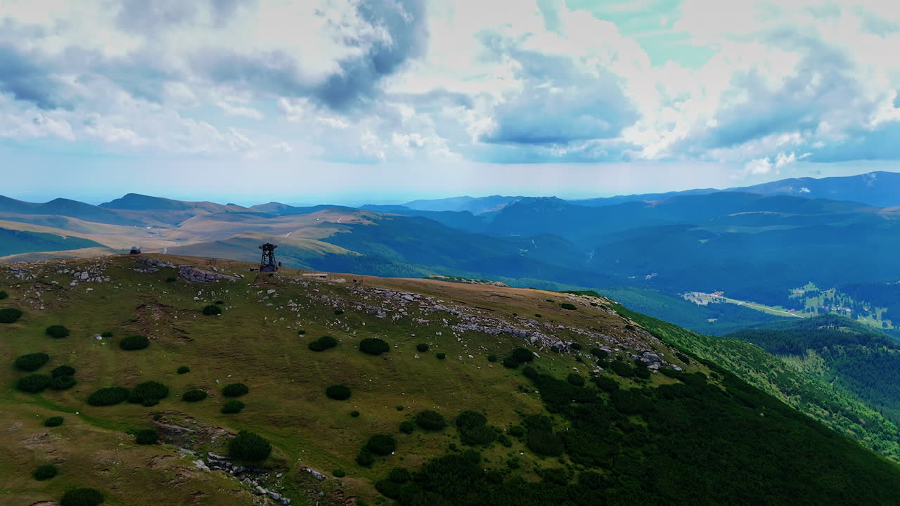 Wide alpine landscape with rolling peaks. Green pastures cover the slopes under a cloudy sky