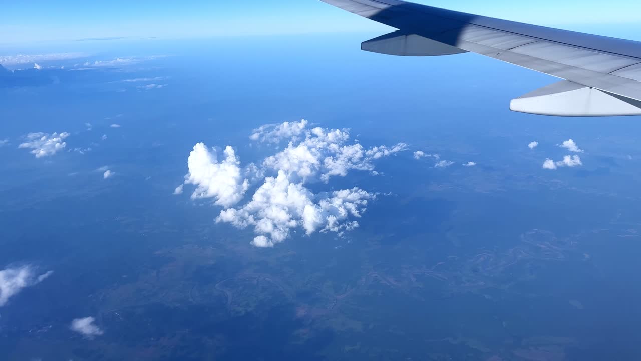 Fluffy white cloud clusters float over vast green terrain—captured mid-flight from an airplane. Ideal for travel, aviation, nature, and sky-themed visuals