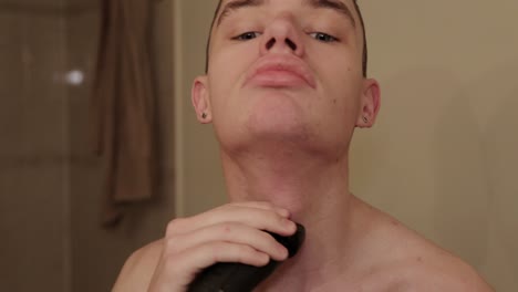un joven se afeita el pelo de la barbilla y el cuello con una maquinilla de afeitar eléctrica