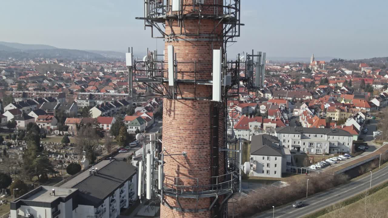 A high-angle aerial view of a tall brick industrial chimney surrounded by a residential neighborhood with red-roofed houses.