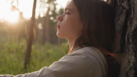 sad lady rests leaning on tree trunk in forest. distressed young woman reflects on idea of psychology help to cope with life challenges. lady with closed eyes feels emptiness