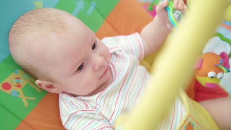 Fröhliches-Baby,-Das-Auf-Einem-Bunten-Bett-Liegt.-Kleiner-Junge,-Der-Spielzeug-Spielt