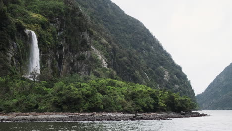 una cascada pacífica se ve desde el agua rodeada de exuberante vegetación en el sonido dudoso, nueva zelanda
