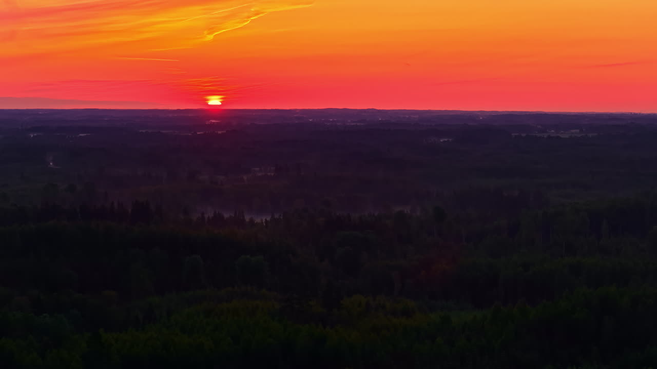 Aerial truck left movement captures a vivid sunset with orange and pink skies above Latvia’s expansive forest landscape