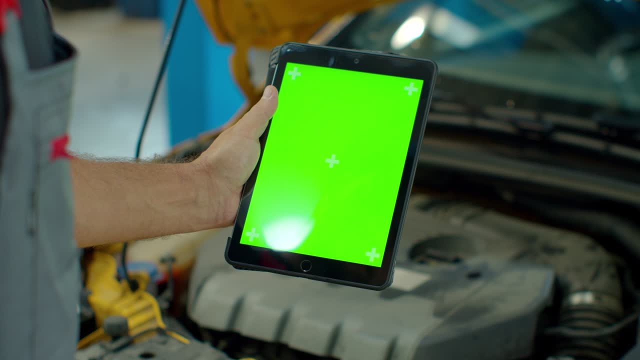 el gerente de servicio de automóviles o el mecánico utiliza una tableta con una maqueta de pantalla verde que está apuntada a una bahía de motores.