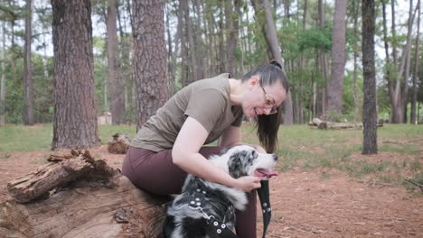 woman sitting on a tree trunk petting her australian shepherd dog