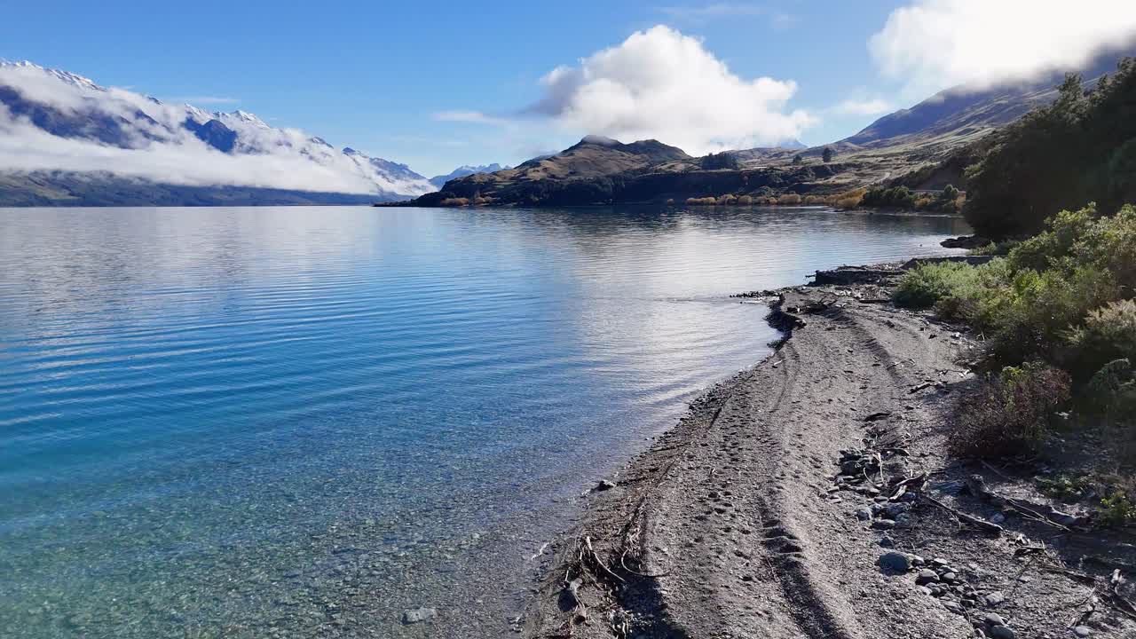 Aerial view of Lake Wakatipu's serene waters and surrounding mountains under clear skies in Glenorchy, New Zealand