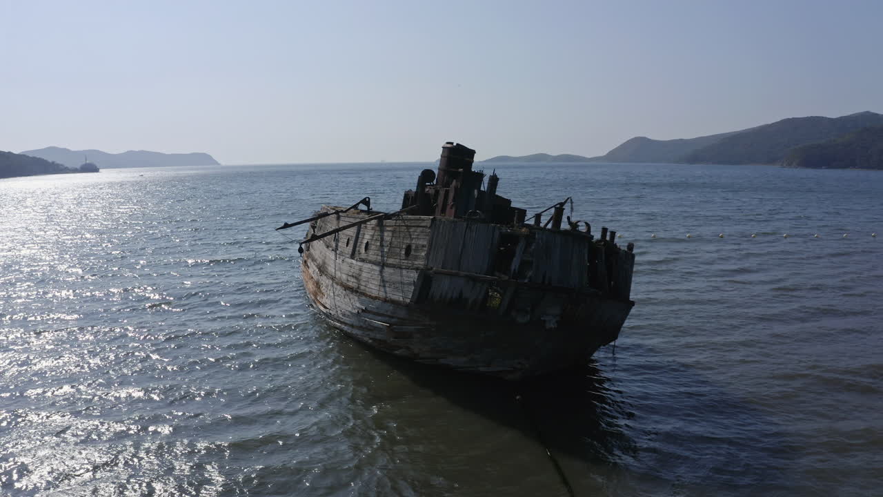Ships graveyard. Slow pivot around the stern of a derelict partially submerged shipwreck, inclined on its starboard side, aground near the shore.