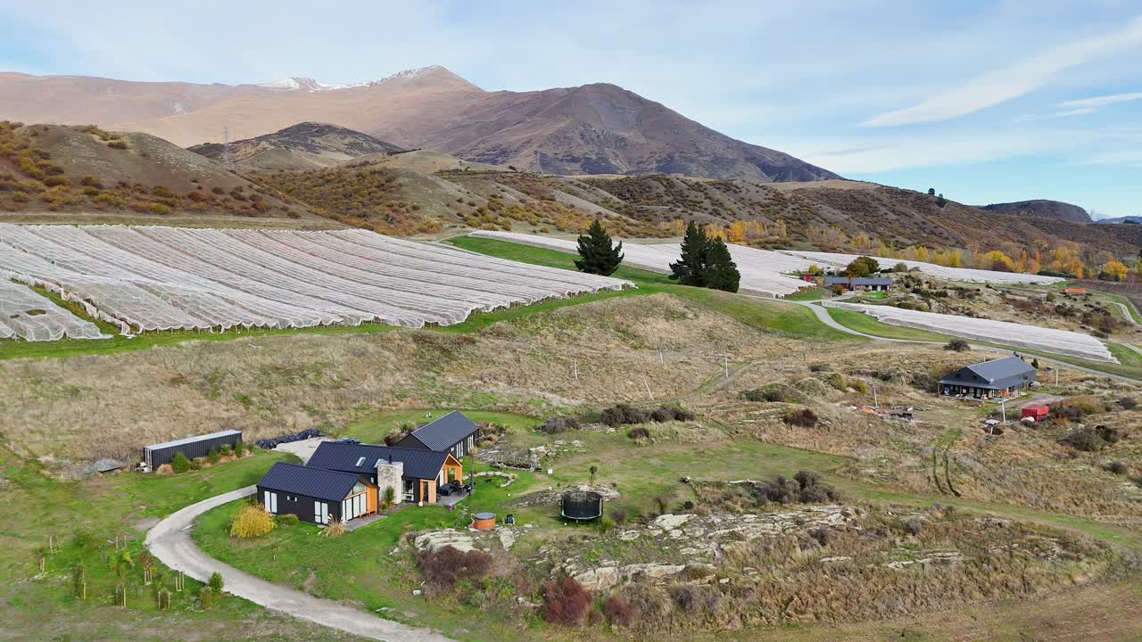 Drone footage captures a scenic vineyard and surrounding landscape in Queenstown, New Zealand, with mountains and clear skies