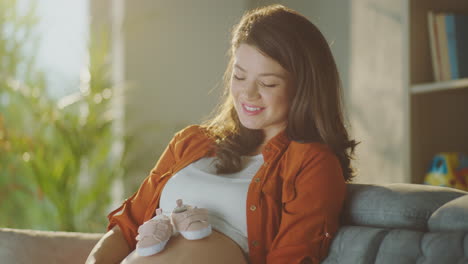 happy pregnant woman looking at baby shoes on belly