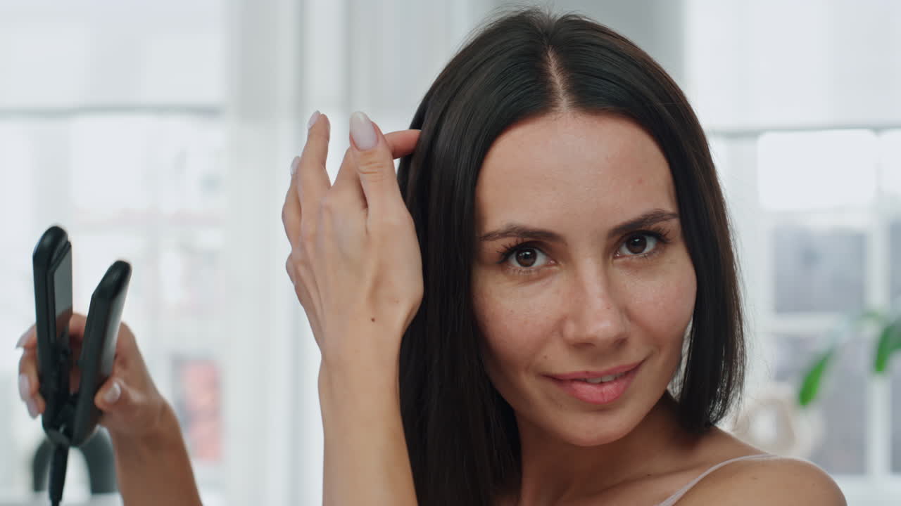 pov chica feliz planchando el cabello en el baño blanco. mujer de primer plano haciendo peinado