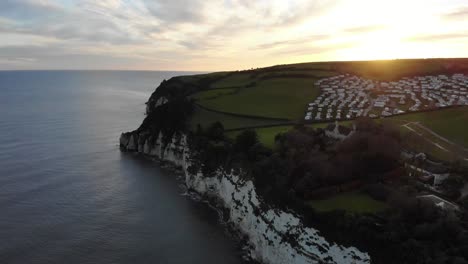 Toma-Aérea-Lenta-De-4k-Sobre-El-Mar-Y-Los-Acantilados-Que-Exponen-La-Hermosa-Puesta-De-Sol-Sobre-La-Ciudad-De-La-Cerveza-En-Devon,-Inglaterra