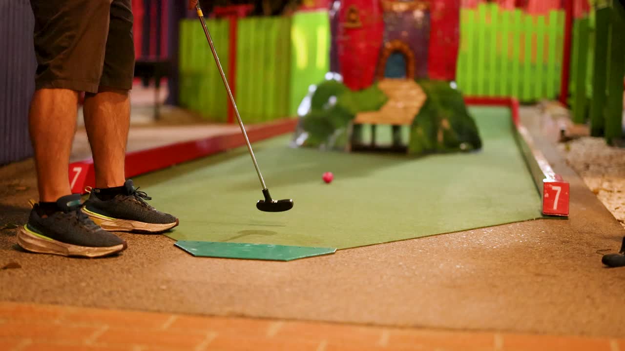 A person attempts a putt on an indoor mini-golf course, missing the hole. Bright colors and playful setting enhance the fun atmosphere