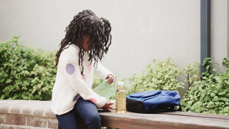 young girl sitting outdoors, enjoying lunch with backpack and juice bottle, copy space