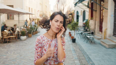 Happy-woman-in-wireless-earphones-dancing,-listening-music-in-smartphone-dancing-walking-city-street