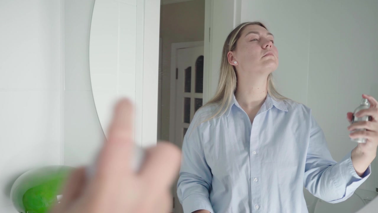 Candidata con una camicia chiara usa uno spray idratante per il viso davanti a uno specchio come parte della sua routine di preparazione per il colloquio.