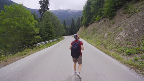 Hombre-Caminando-Por-Una-Carretera-Asfaltada-En-El-Bosque.