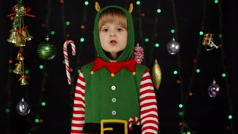 Kid-girl-in-Christmas-elf-Santa-Claus-helper-costume-holding-finger-near-lips-for-silence,-hush-sign