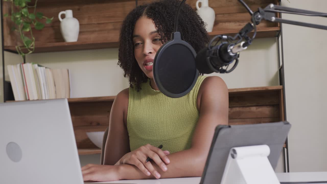 African American woman typing, leaning into mic, podcasting, speaking at desk using laptop tablet