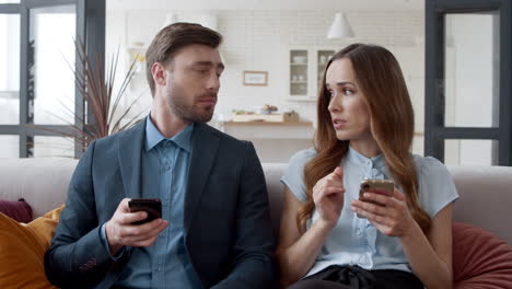 Young-woman-talking-to-husband-at-home.-Couple-browsing-internet-on-phones.