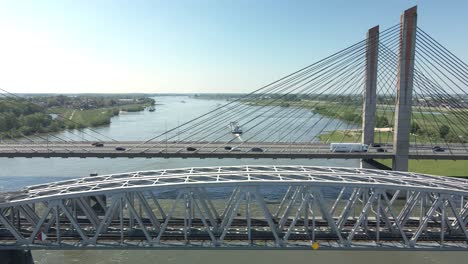 flying parallel to highway bridge and railway bridge with boat crossing the river in the background on a clear sunny day