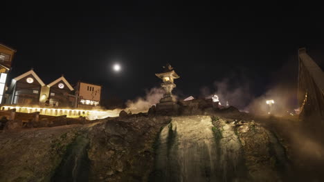 up shot of a japanese stone lantern on top of a steaming hot spring waterfall in kusatsu onsen village in the evening after light up