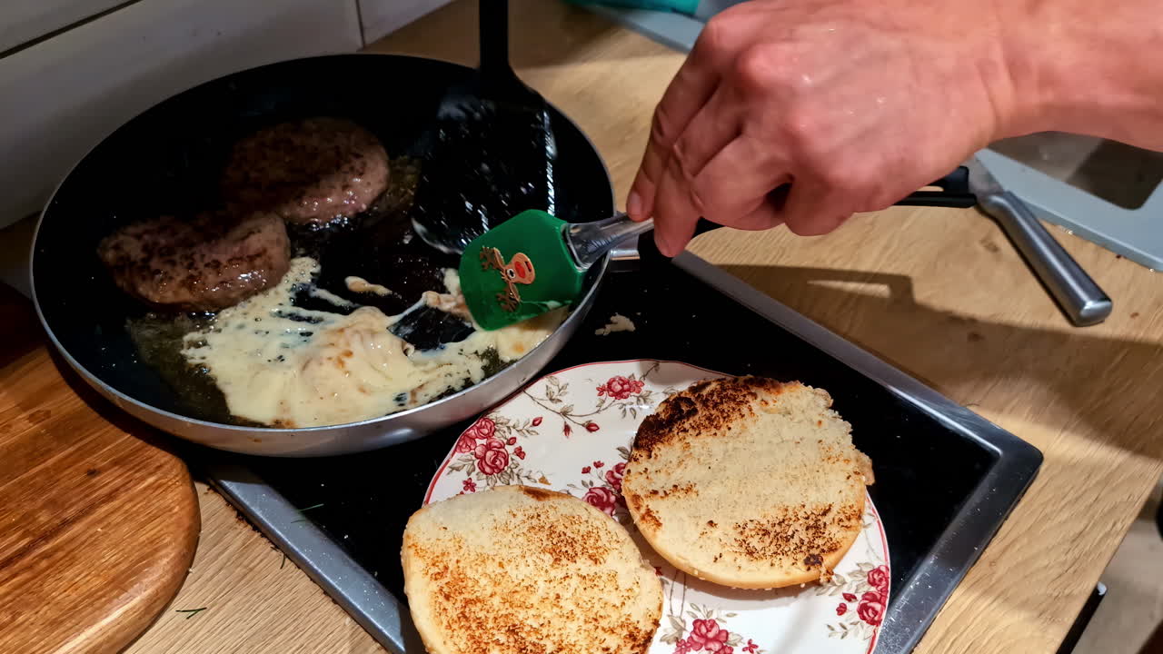 Burger patties cook with cheese, while toasted buns sit ready on a plate