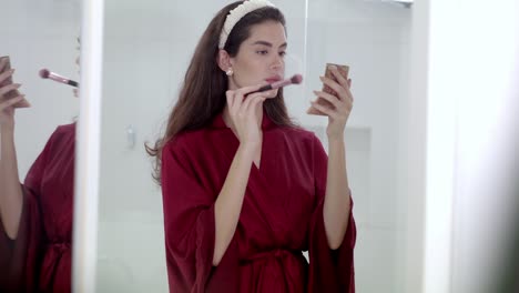 joven mujer atractiva hace uso de pequeño maquillaje compacto y set de pinceles
