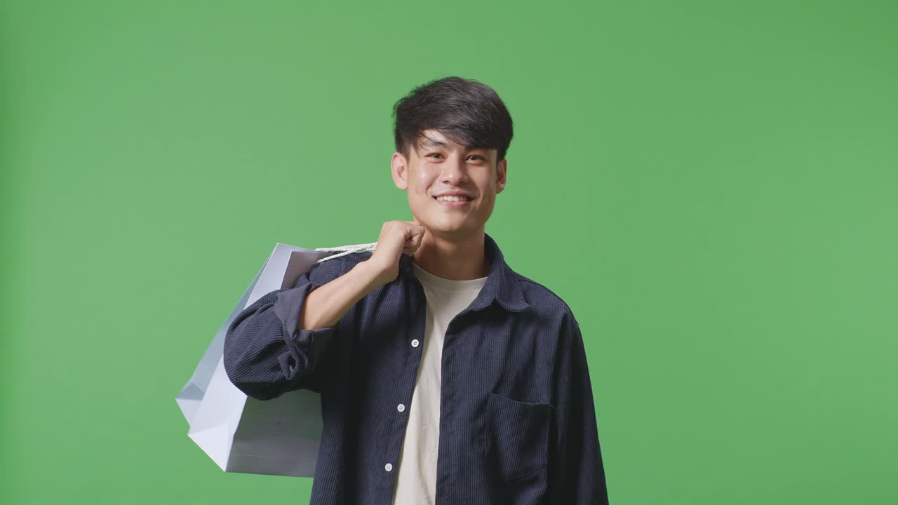 ショッピングバッグを持ったアジア人ショッピングマンが笑顔でグリーンスクリーンの前を歩いています