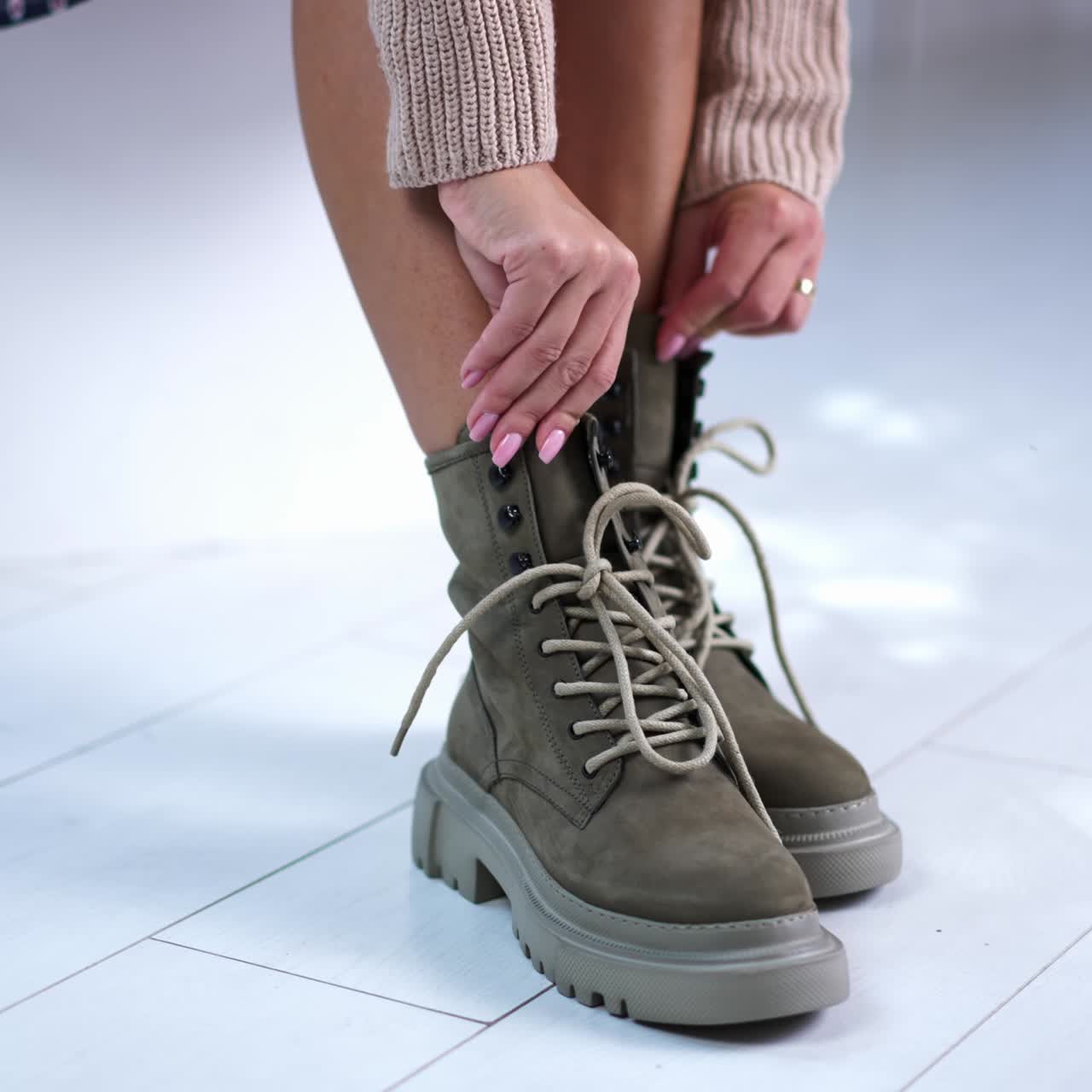 Model ties the laces on the modern boots. Sitting female demonstrating grey fashionable footwear. Close up
