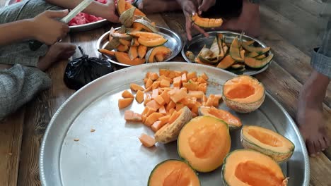 hands of a senior man using two knives to cut fresh delicious cantaloupe muskmelon in big plates, a man cuts a melon into slices, cubes in a plate