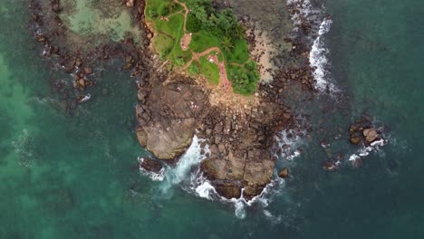 aerial drone birds eye view of tropical island surrounded by rocky shore and blue ocean water in scenic sri lanka