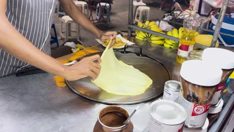 A street vendor skillfully prepares Thai roti on a hot griddle in Phuket, Thailand, showcasing traditional cooking techniques and vibrant street food culture