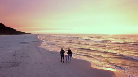 parents walking with a small child on a beach at sunset. happy family enjoying a walk on a beach. sunset beach walk drone footage.
