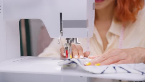 asian beautiful tailor woman working on clothes in tailoring atelier. attractive young female fashion designer pushes fabric material through a sewing machine making new handmade suit in workshop room