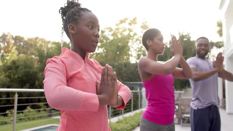 happy african american parents and daughter practicing yoga in sunny garden, in slow motion